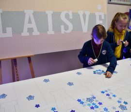 Mokiniai klijuoja neužmirštuoles ant stendo